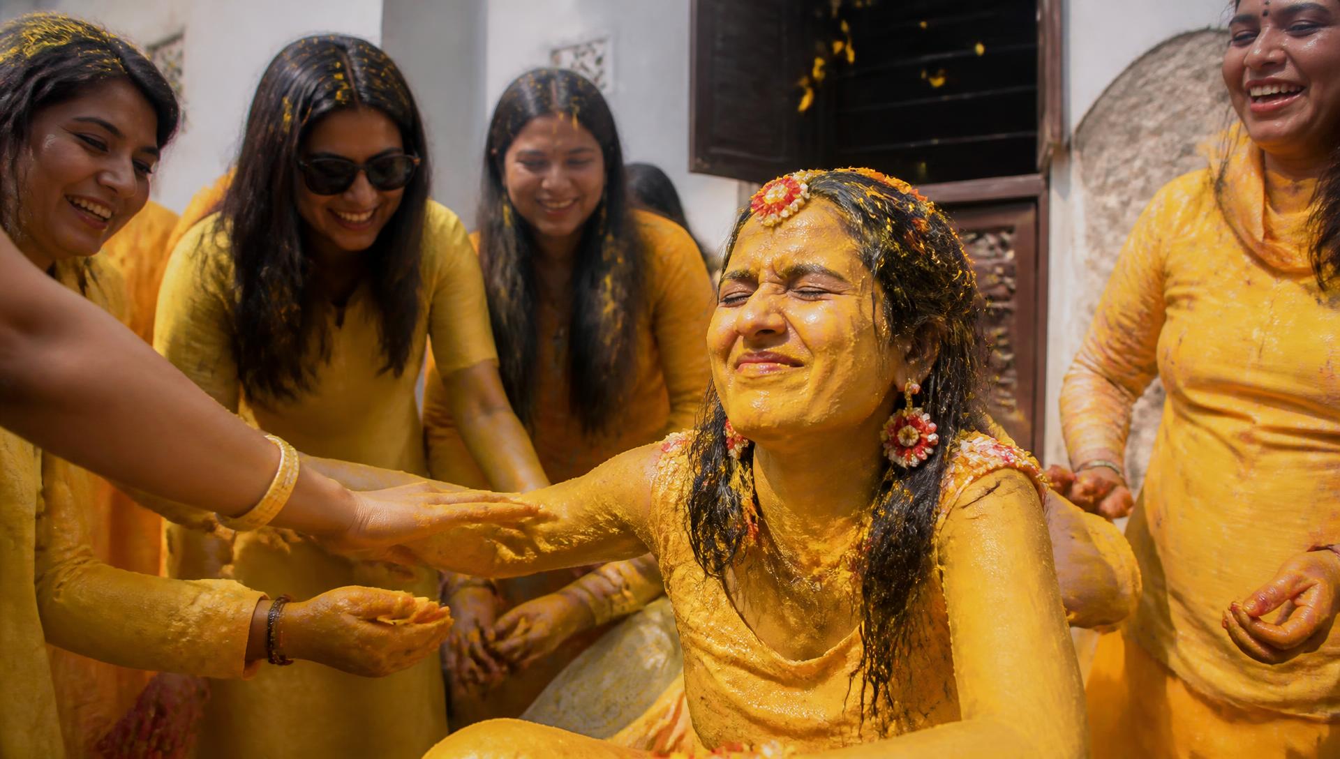 Cousins smearing turmeric on the bride during a haldi ceremony
